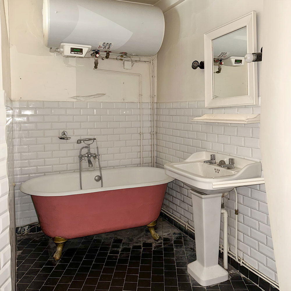 Salle de bain avec ancienne baignoire rouge et chauffe eau au-dessus