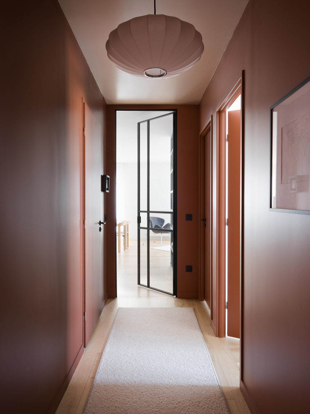Couloir terracotta ouvrant sur le séjour par une porte vitrée noire.