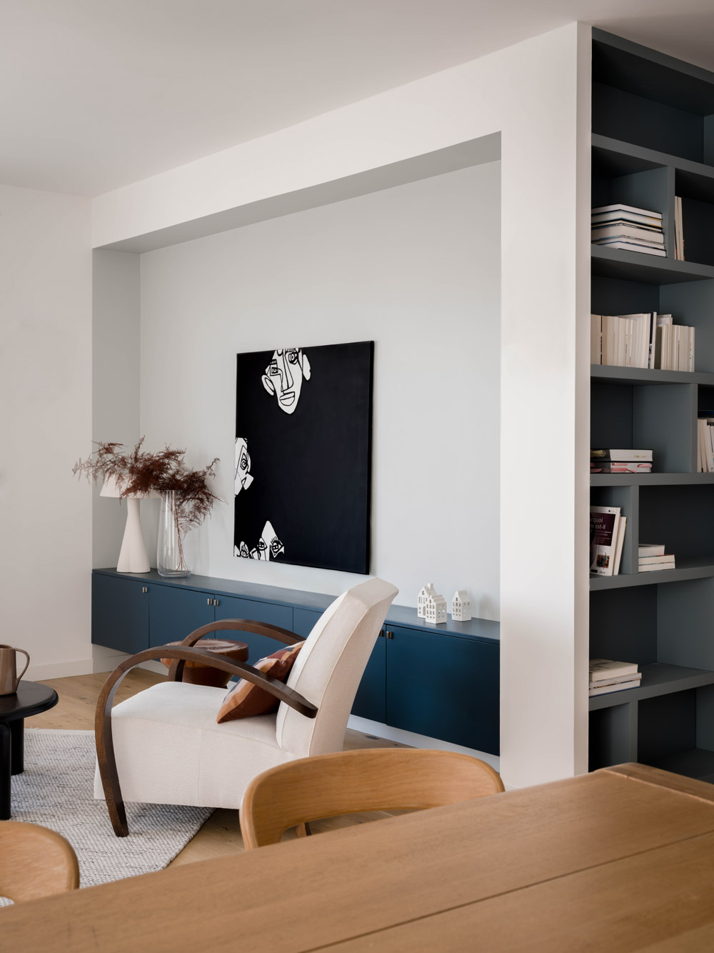 Salon avec bibliothèque sur mesure gris bleu, meuble bas bleu et fauteuil blanc.