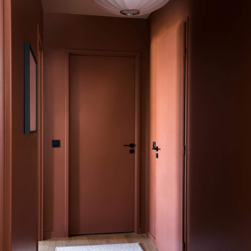 Couloir terracotta avec portes peintes ton sur ton et suspension sculpturale blanche.