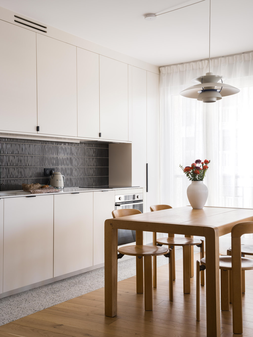 Cuisine blanche sur mesure ouverte sur un espace repas lumineux avec rideaux légers.