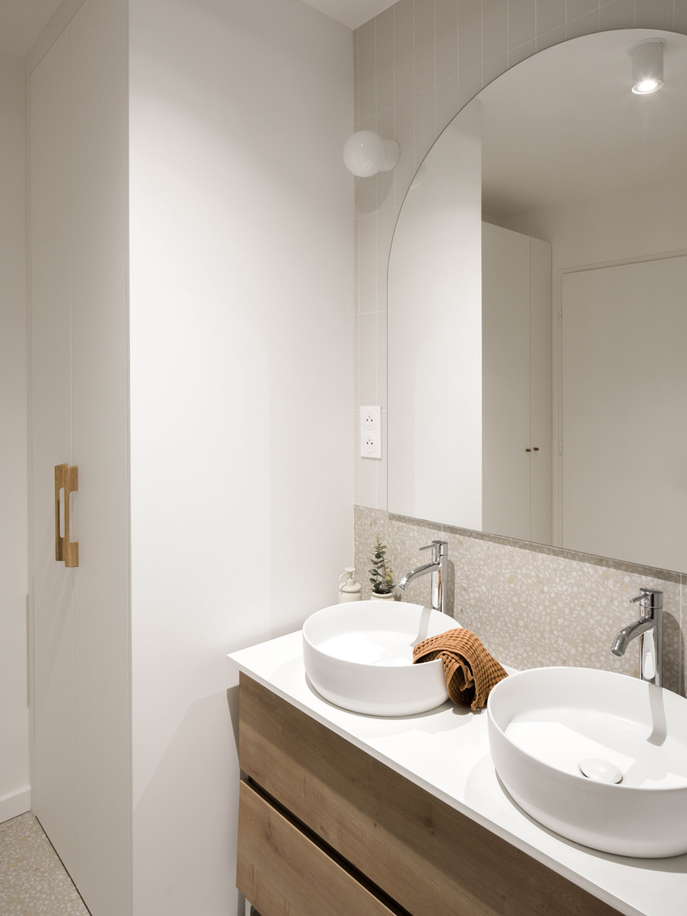 Salle de bain avec double vasque, miroir en arche et meuble bois dans un appartement rénové.